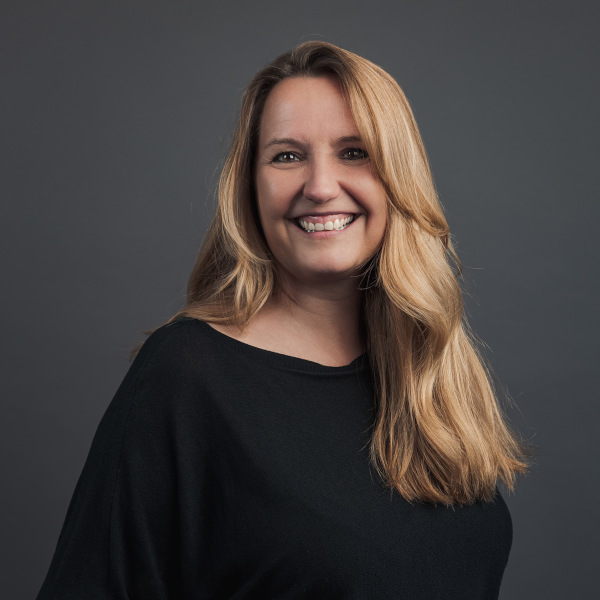 anja middelkamp, head of projektmanagement bei friederbarth, porträtfoto mit langen blonden haaren und schwarzem oberteil vor dunkelgrauem hintergrund