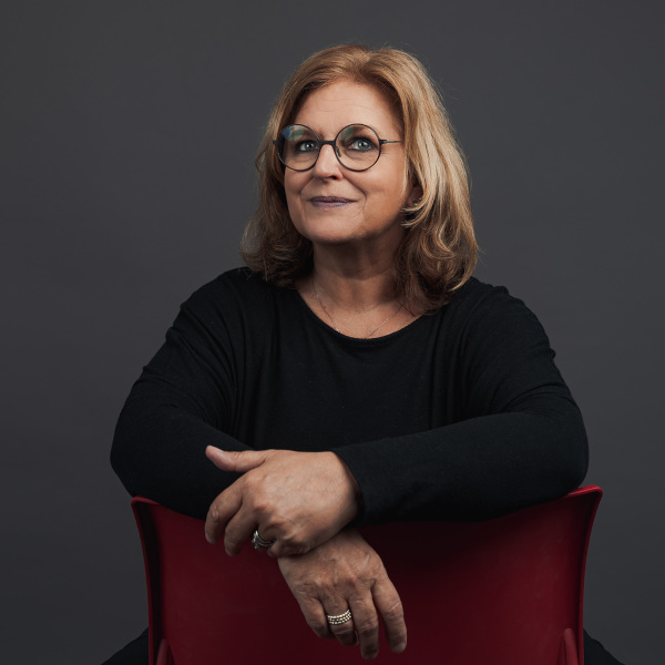 gaby hinrichs, premium professional bei friederbarth, porträtfoto mit blonden haaren im schwarzen oberteil auf rotem stuhl
