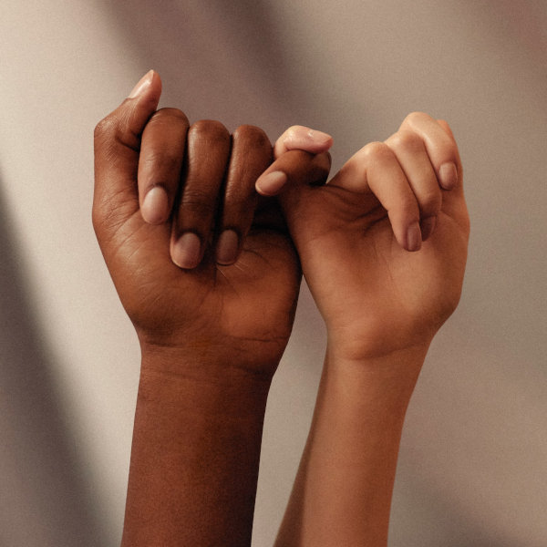 Zwei Hände mit unterschiedlichen Hauttönen verschränken die kleinen Finger – Symbol für Vertrauen, Verbindung und Vielfalt
