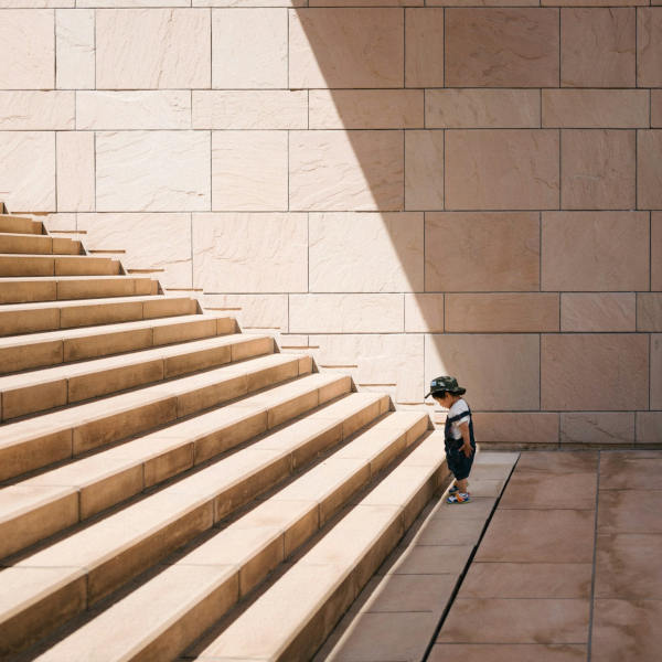 Ein kleines Kind steht am Fuß einer breiten Steintreppe und blickt nach oben – symbolisch für den Beginn eines Lernprozesses und den Weg zu praxisnahen Lösungen im Coaching.