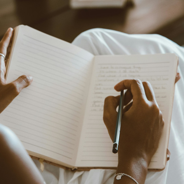 eine Person schreibt mit einem Stift in ein liniertes Notizbuch – Fokus auf Hand und Buch, unscharfer Hintergrund