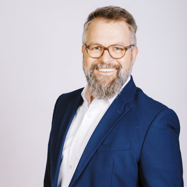 Alexander Wolf im blauen Anzug mit weißem Hemd – Portraitaufnahme mit unscharfem Gesicht vor hellem Hintergrund