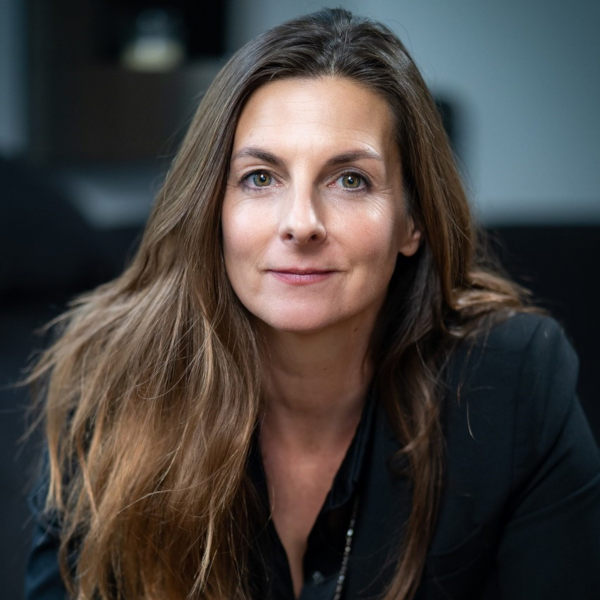 Carolin Schmidt mit langen braunen Haaren im dunklen Blazer – Portraitaufnahme mit unscharfem Gesicht in Innenraum mit unscharfem Hintergrund