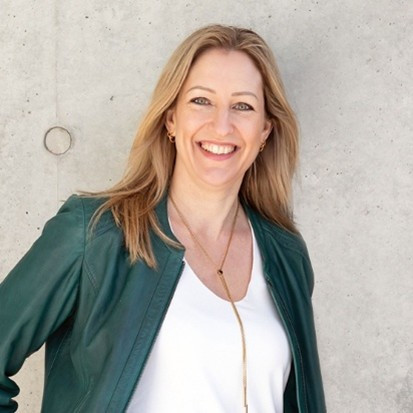 Katharina Krentz mit langen blonden Haaren in gruener Jacke und weißem Shirt – Portraitaufnahme mit leicht unscharfem Gesicht