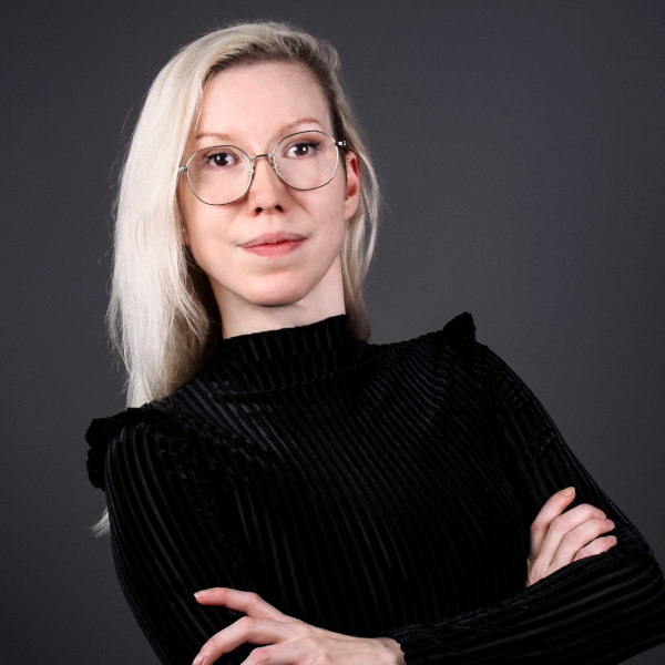 Nell Kindt mit langen, hellen Haaren im schwarzen Rollkragenpullover – Portraitaufnahme mit unscharfem Gesicht vor dunklem Hintergrund