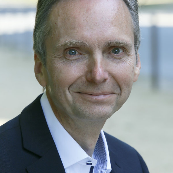 Volker Helweg in dunklem Anzug und weißem Hemd – Portraitaufnahme mit unscharfem Gesicht