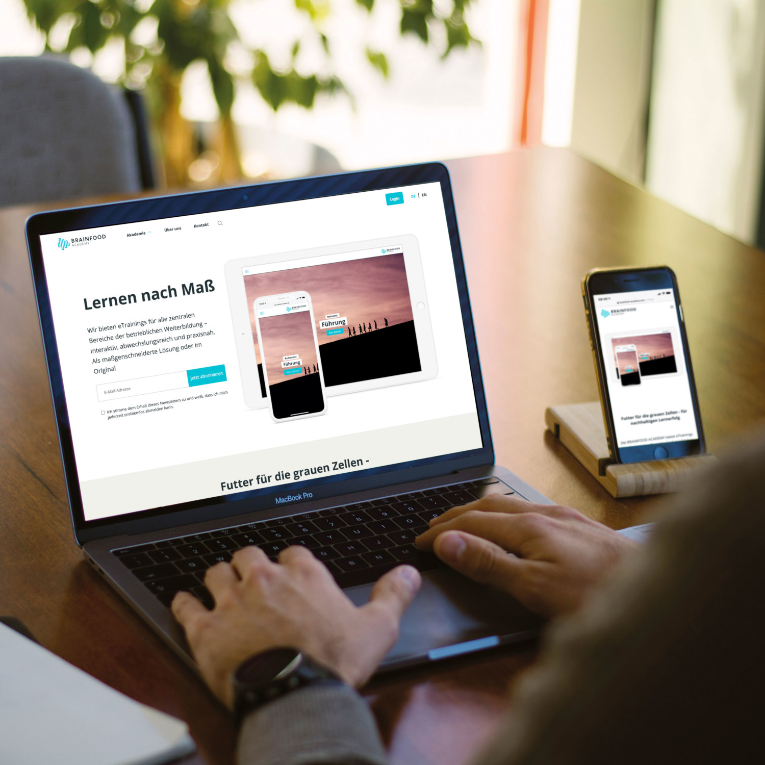 Person nutzt Laptop und Smartphone mit geöffneter Brainfood Academy Website, die digitale Lerninhalte für berufliche Weiterbildung zeigt
