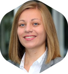 Person mit blondem Haar, weißem Hemd und grauem Blazer vor verschwommenem Innenraum – symbolisch für motivierende Zusammenarbeit und Konzeptentwicklung bei expert.