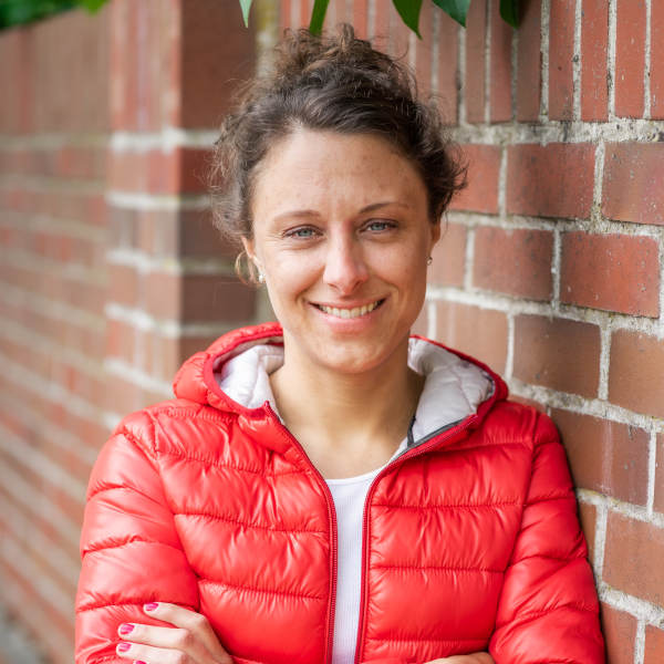 Hanna Selm, systemische Beraterin und Coach, vor Backsteinwand im Outdoor-Setting – Expertin für Organisationsentwicklung und Führungskräfteentwicklung